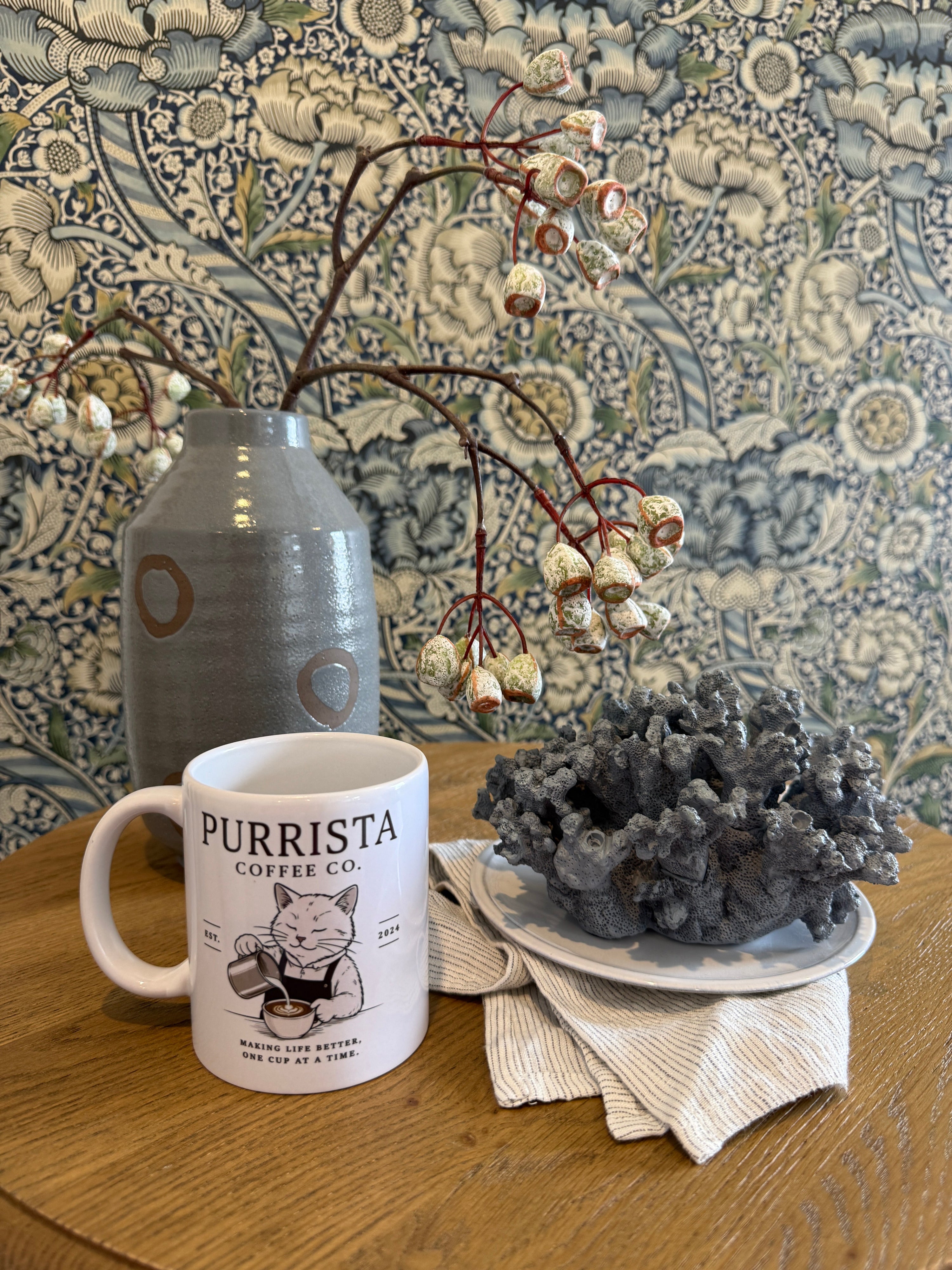 Purrista Coffee Co. mug on a wooden table with decorative elements and patterned wallpaper.